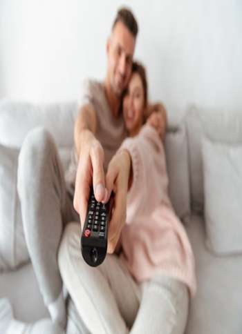 Smiling loving couple sitting on couch together and watching TV. Focus on TV remote